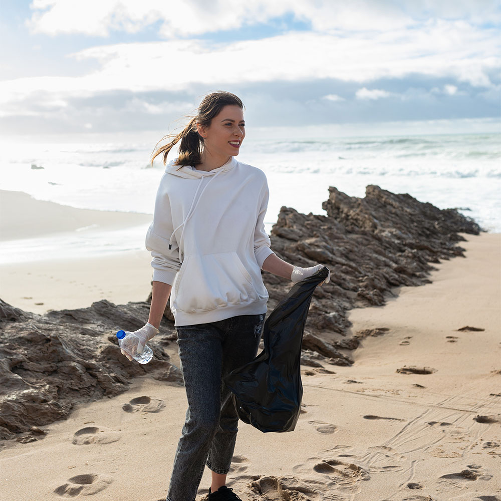 A woman picking up recyclable waste on a beach, engaged in environmentally friendly practices and promoting sustainability through recycling efforts