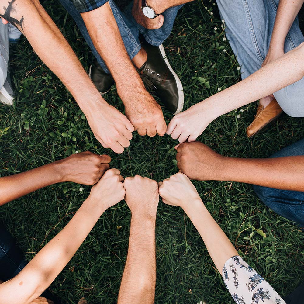 A diverse group of people standing in a circle, joining their fists together in unity and solidarity, symbolizing teamwork and collaboration